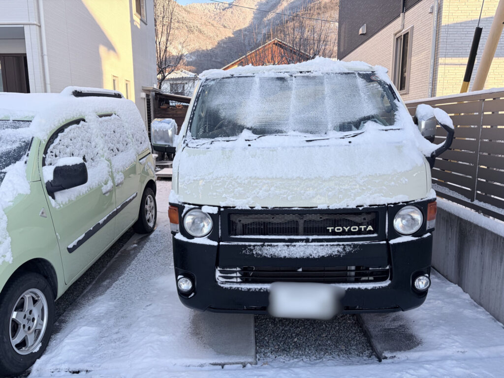 雪が積もったライトイエローのハイエース200系。丸目ヘッドライトとブラックフロントを正面から撮影